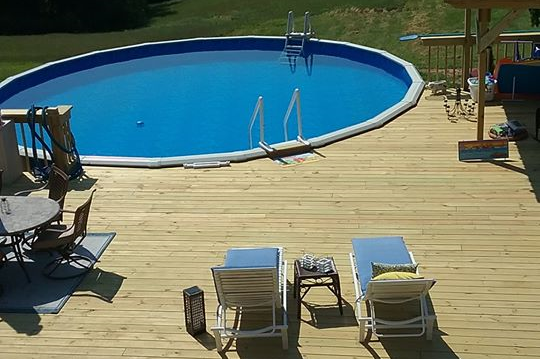 In-ground pool with lounge chairs on a wooden deck surrounded by trees
